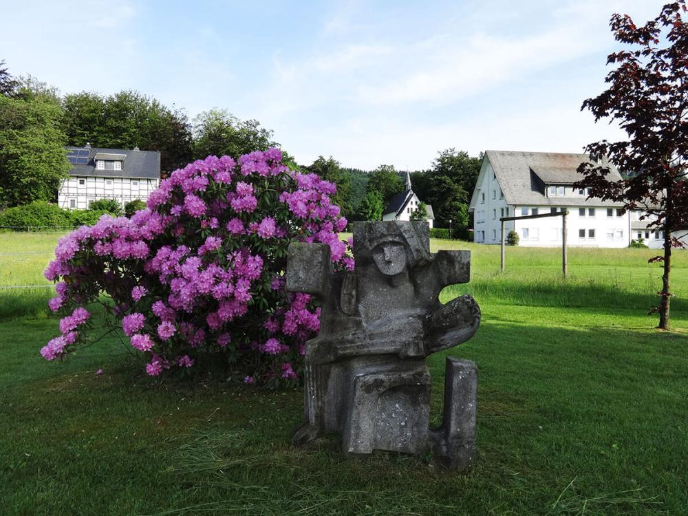 Steinskulptur neben blühendem Strauch