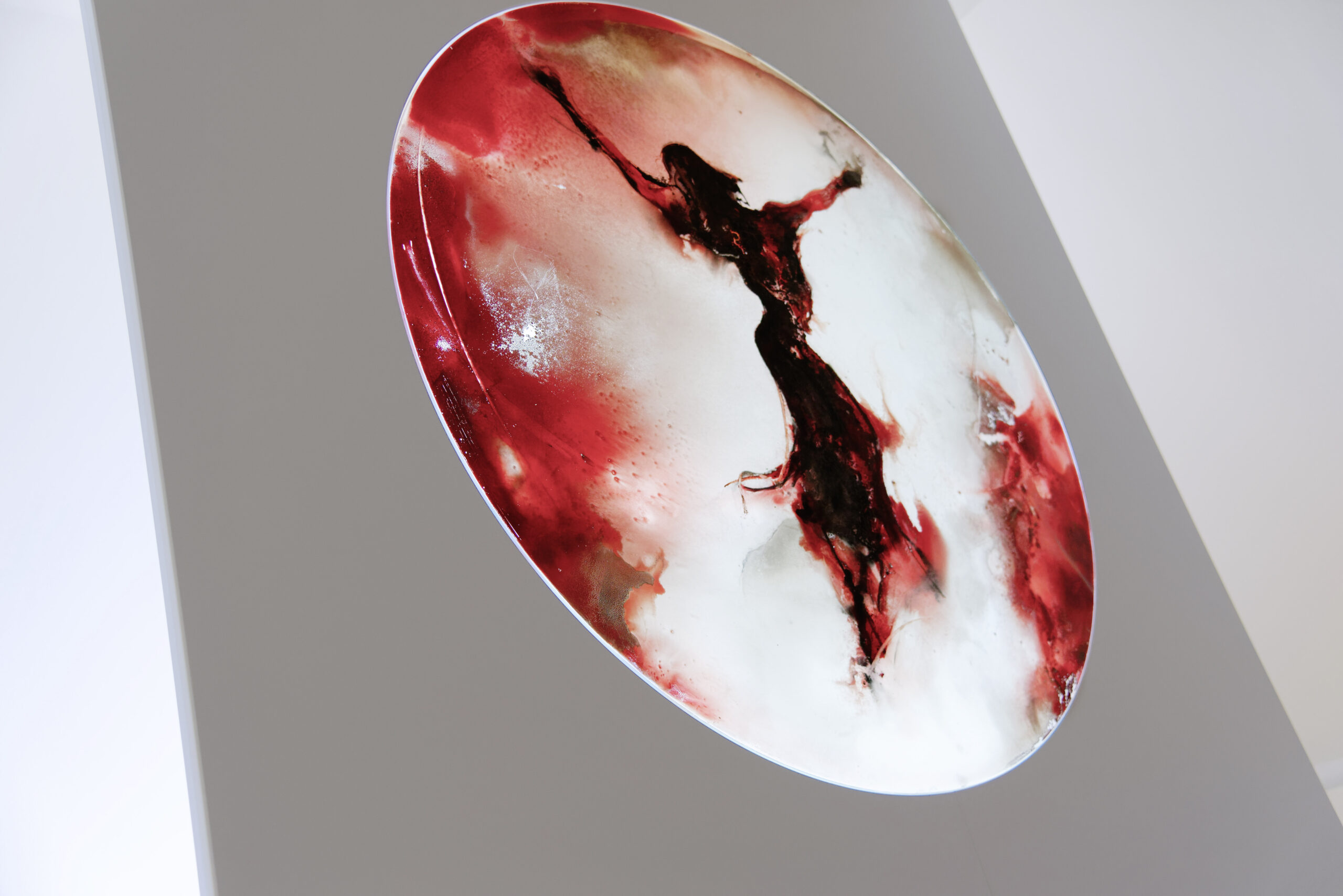 Rundes künstlerisches Glasbild mit abstrakter Darstellung einer Figur in Rot- und Weißtönen.