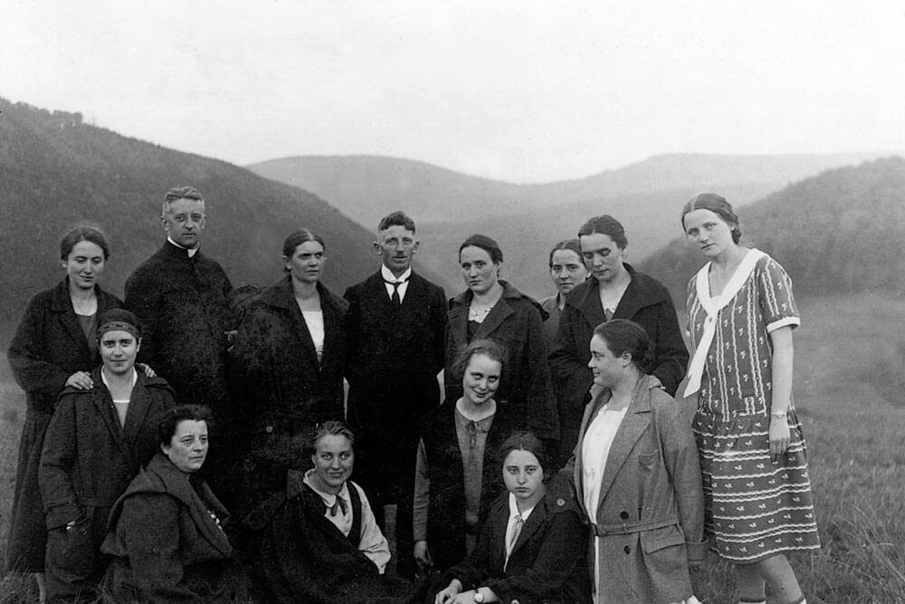Historisches Schwarz-Weiß-Foto einer Gruppe von Menschen in Landschaft, vermutlich frühes 20. Jahrhundert.