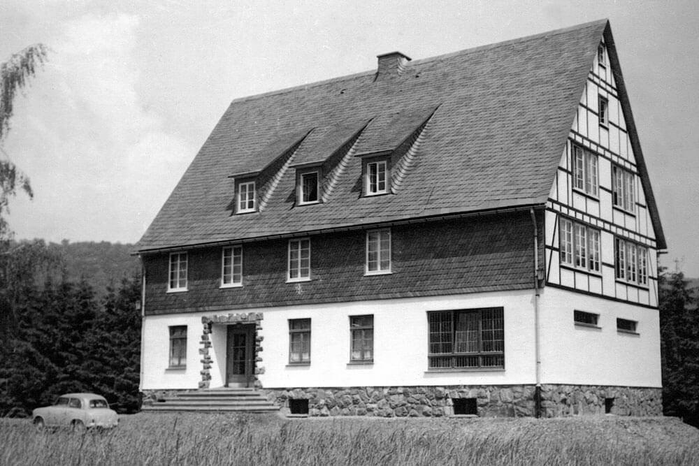 Historisches Schwarz-Weiß-Foto eines Hauses im Fachwerkstil in ländlicher Umgebung.