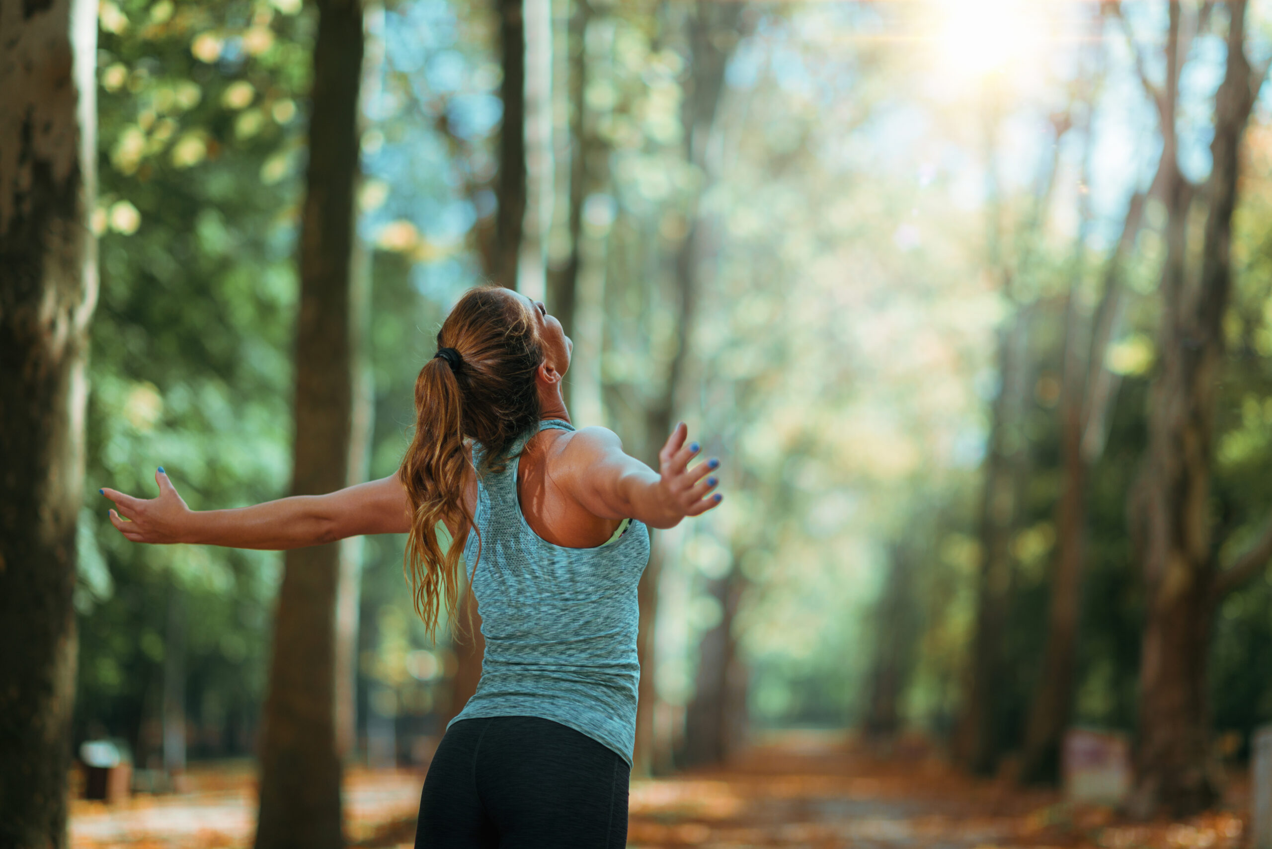 Eine Frau, die im Wald ihre Arme öffnet.