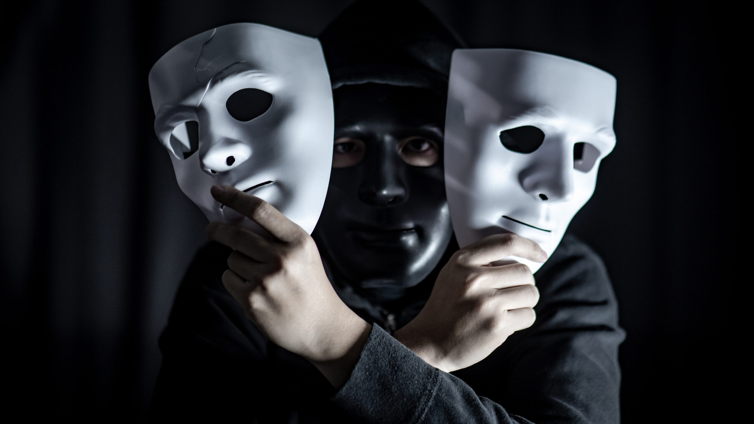 Zwei Hände, halten zweit weiße Masken und in der Mitte ein schwarzes Gesicht