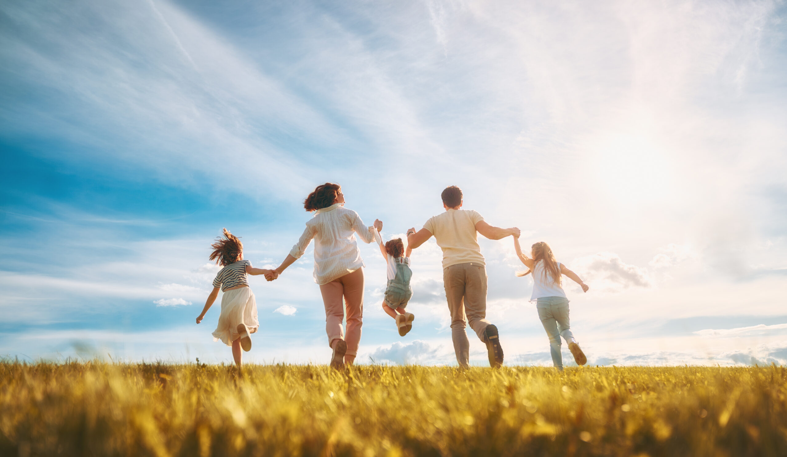 Eine Familie: Mutter, Vater und drei Kinder hüpfen fröhlich übers Feld