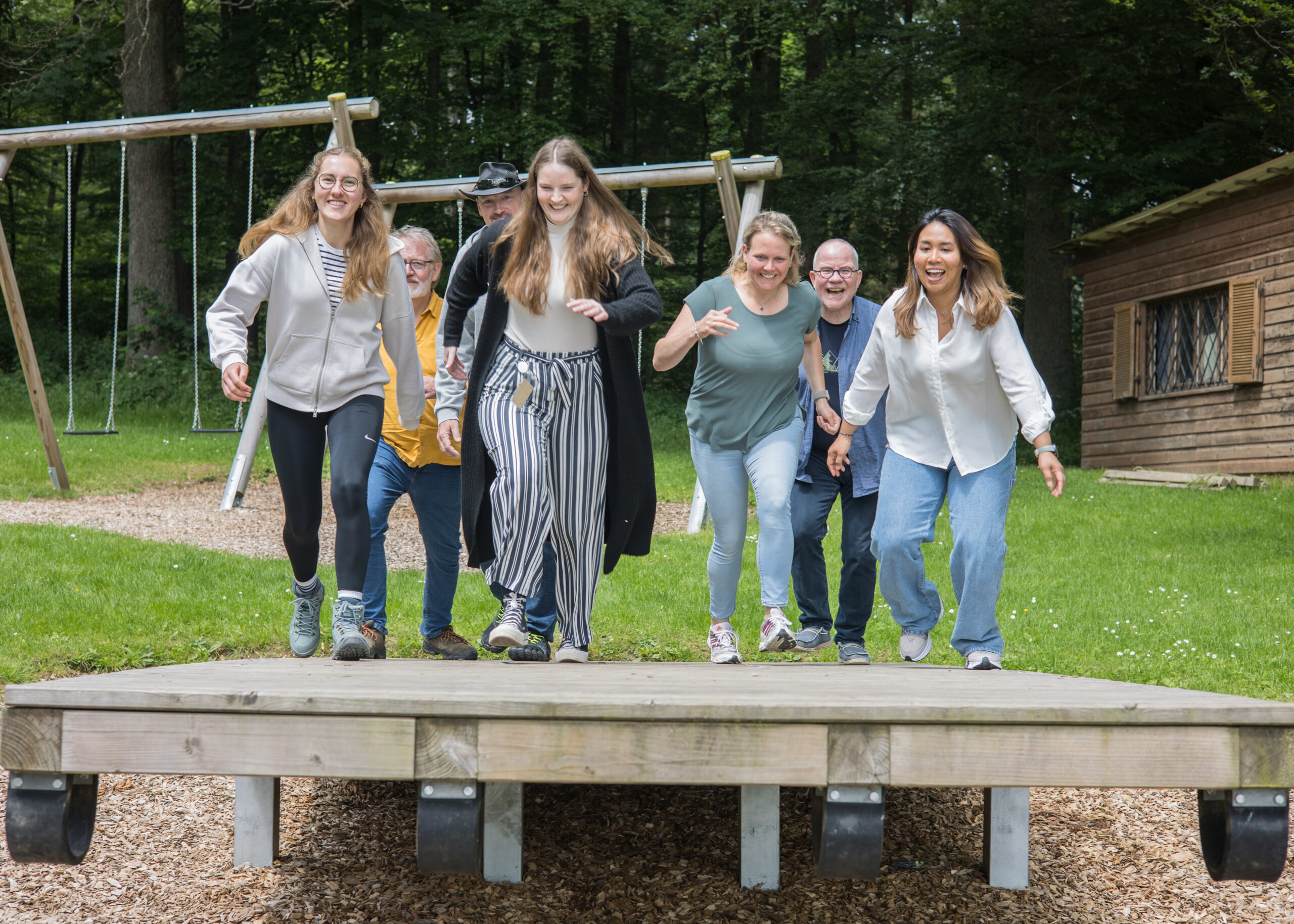 Sieben Männer, Frauen und Jugendliche auf einer Teamwippe auf dem Spielplatz