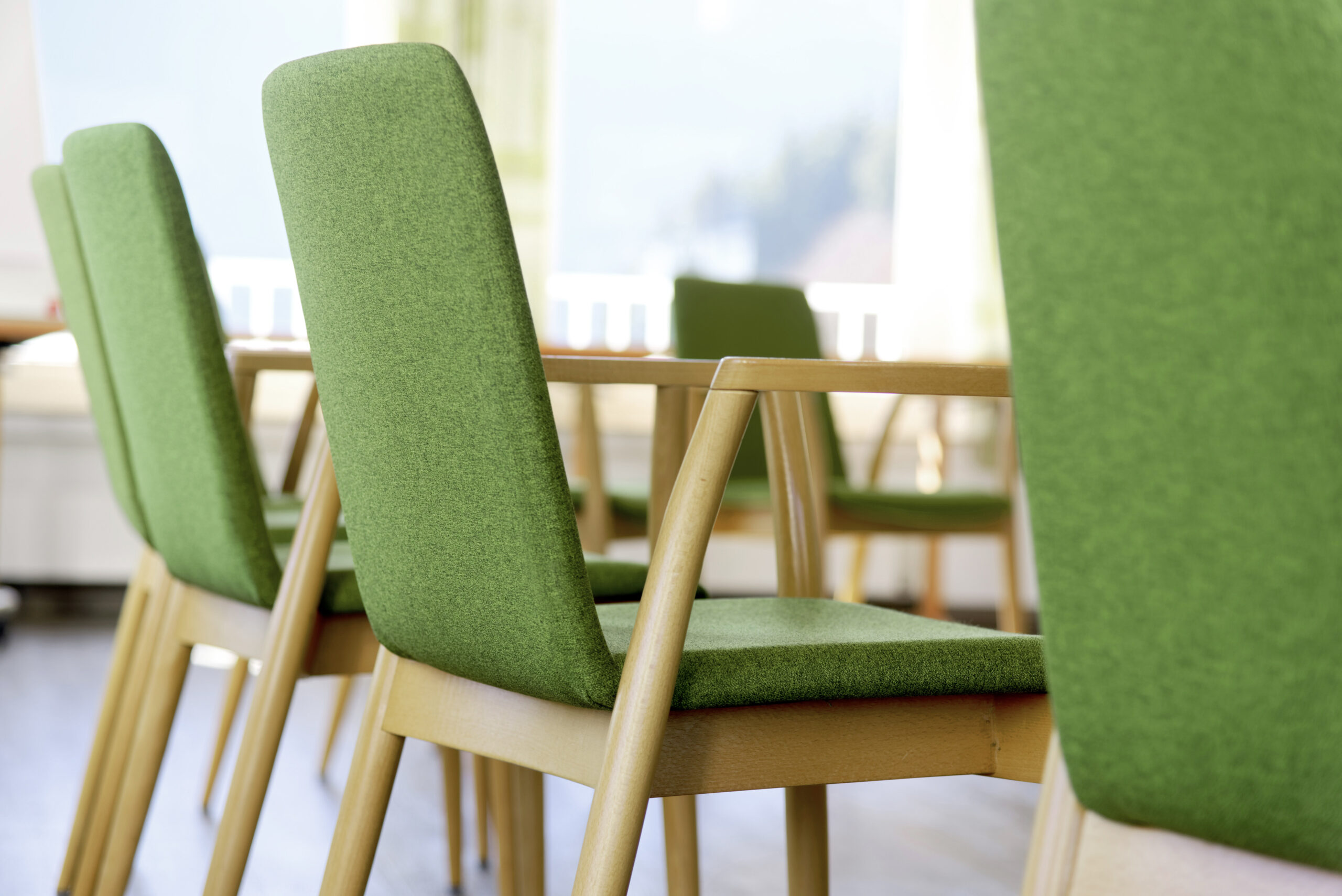 Grün gepolsterte Stühle an einem Besprechungs- oder Seminarraumtisch in heller und moderner Atmosphäre.