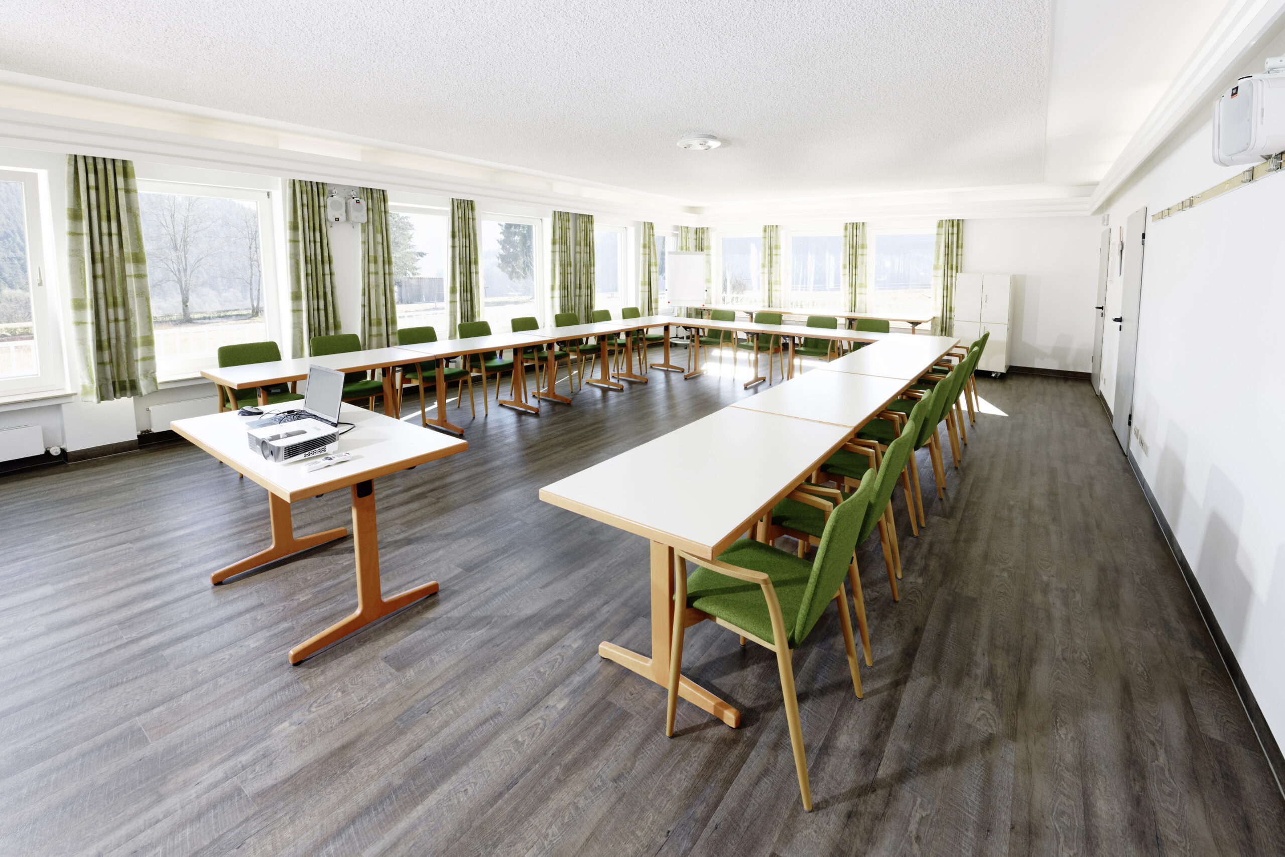 Großer Seminar- und Tagungsraum mit U-förmig angeordneten Tischen, grünen Stühlen sowie Präsentationstechnik für Workshops und Besprechungen.