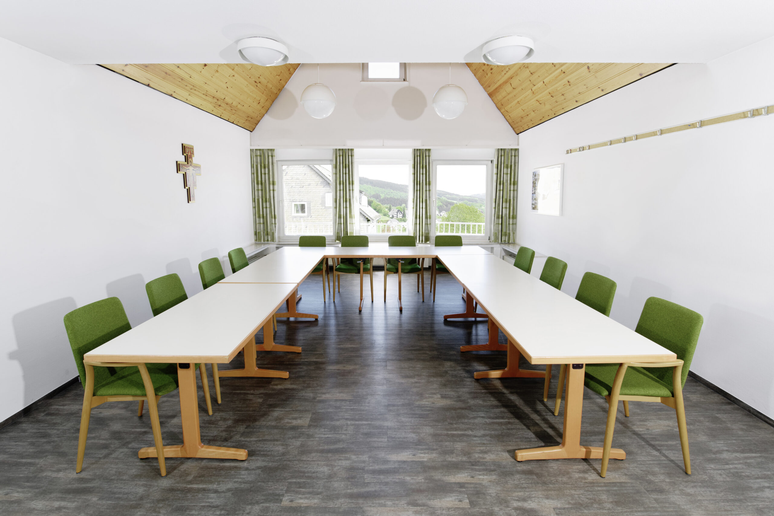 Kleiner Seminarraum mit U-förmig angeordneten Tischen, grünen Stühlen und Tageslicht für Besprechungen, Workshops und Gruppenarbeiten.