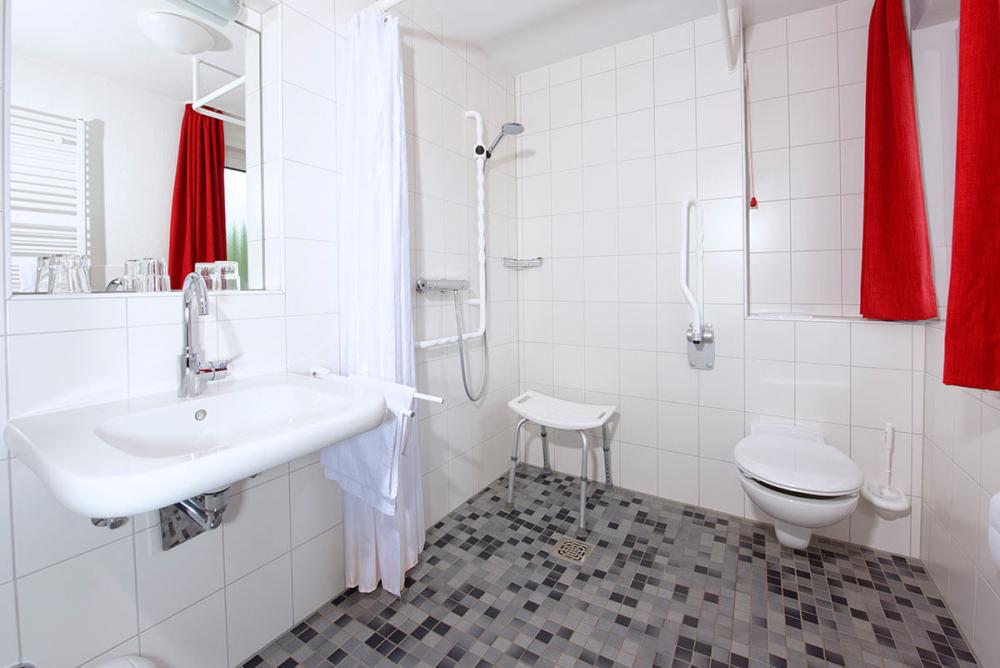 Weißes Badezimmer mit Toilette, barrierefreier Dusche, Waschbecken und Spiegel