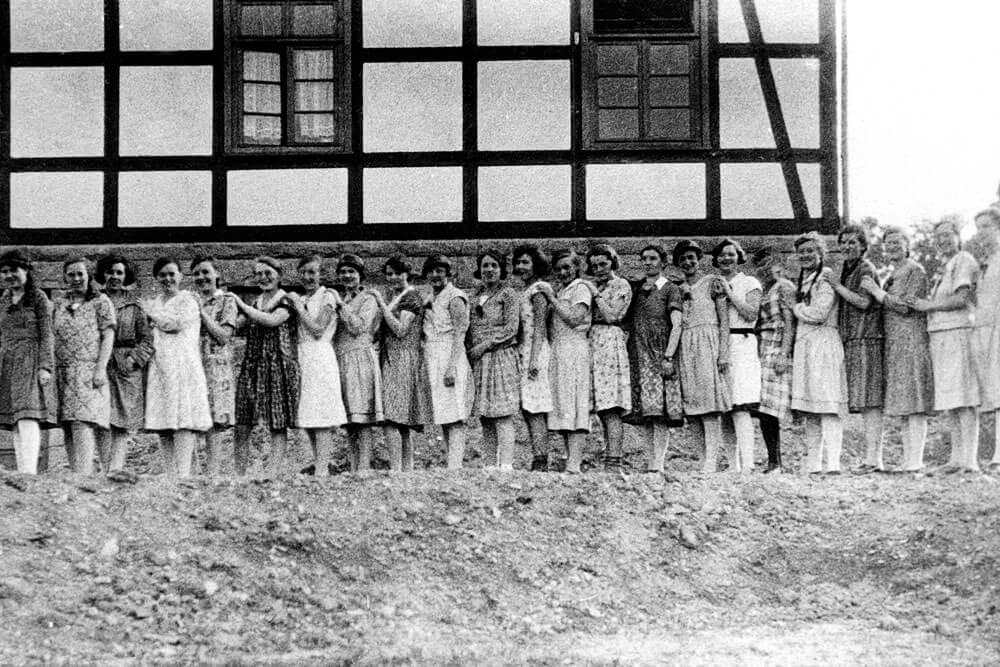 Historische Schwarz-Weiß-Fotografie einer Gruppe von Frauen vor einem Fachwerkgebäude.