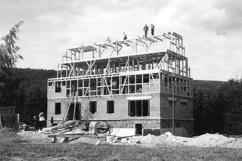 Historische Schwarz-Weiß-Fotografie eines mehrstöckigen Gebäudes im Bau mit Arbeitern auf dem Dachstuhl.