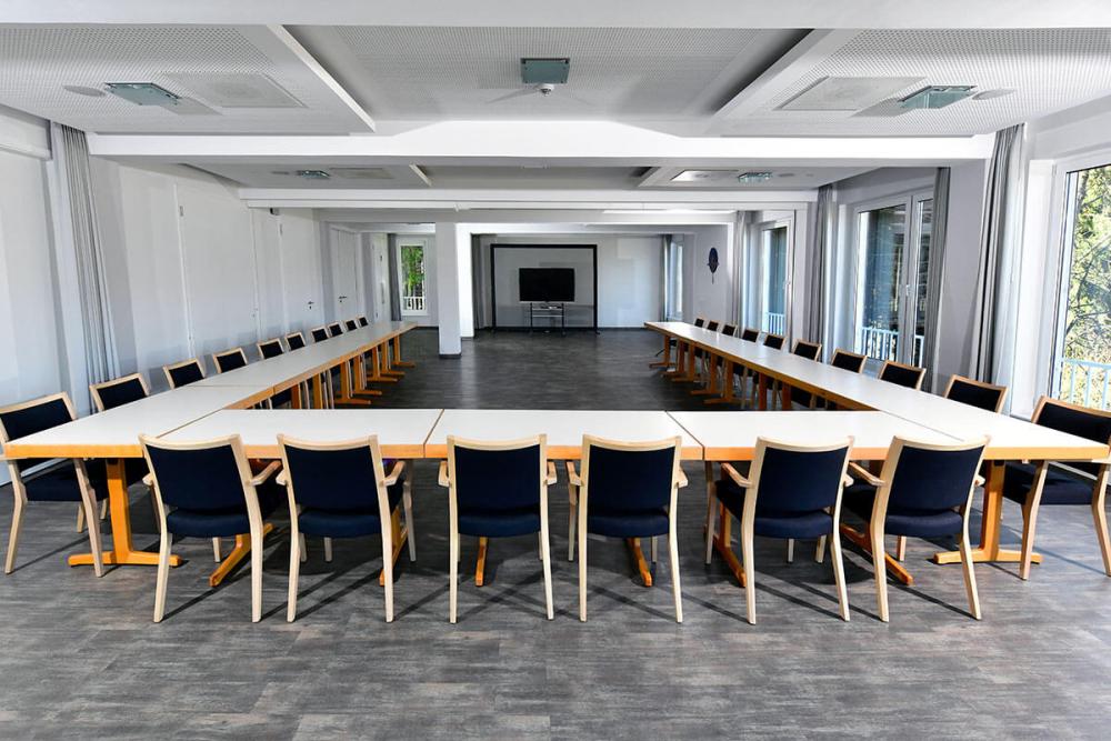 Heller Seminarraum als U-Form gestellt. Hinten ist ein Fernseher sichtbar.